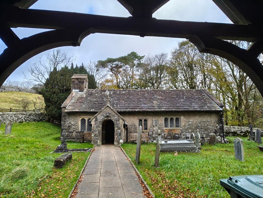 St Leonard's Church features a stone exterior, arched entrance, gravestones, and surrounding trees in a serene landscape.