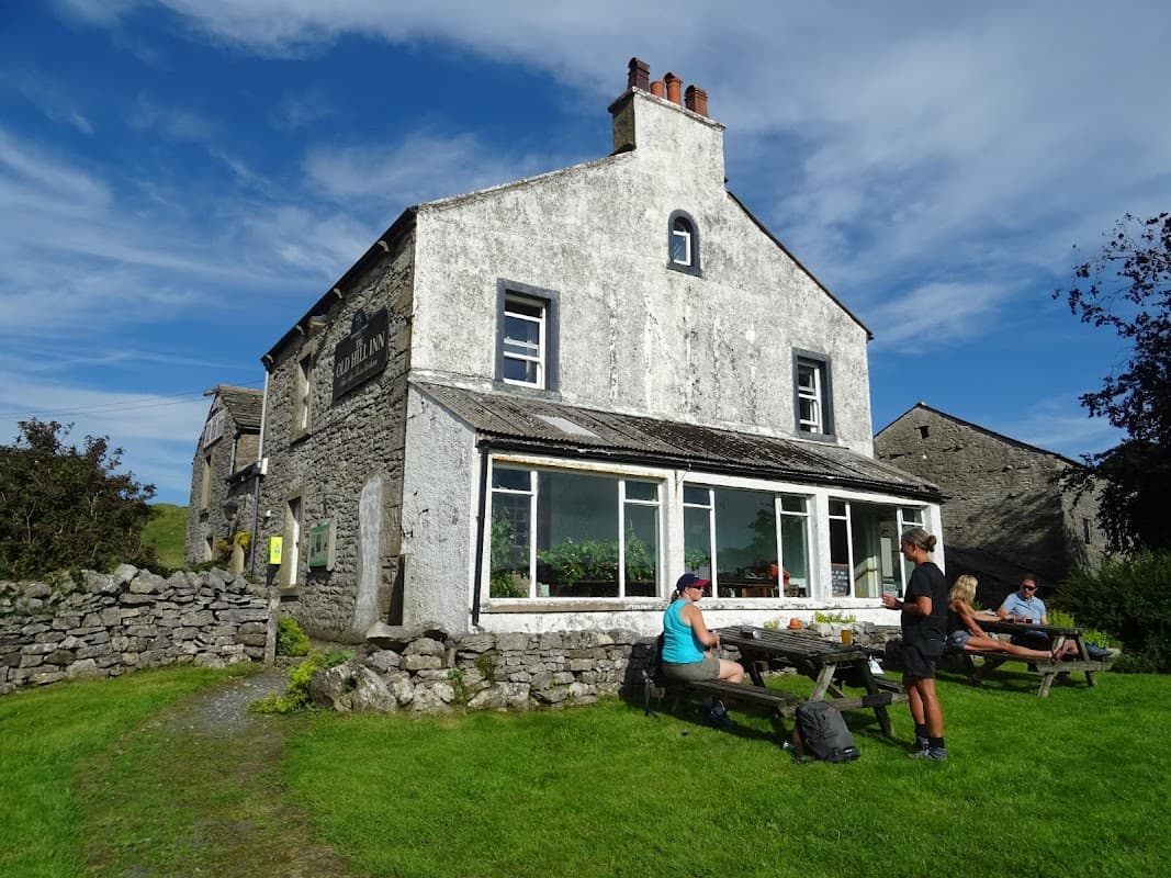 The Old Hill Inn, a stone building with large windows, surrounded by green grass and picnic tables, under a blue sky.