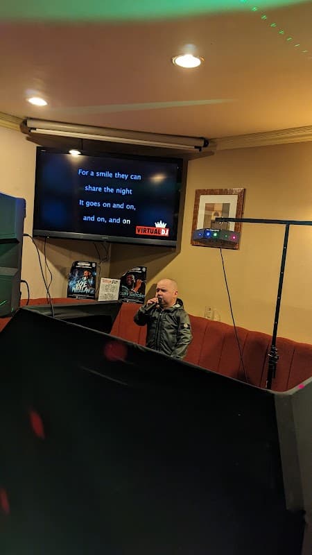 A small stage with a microphone, a karaoke screen displaying lyrics, and colorful lights in a lively atmosphere.