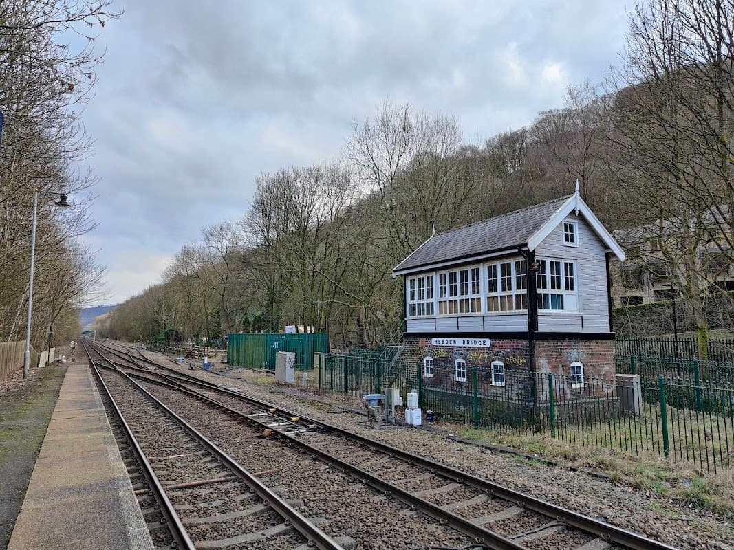 Historic signal box beside railway tracks, surrounded by trees and fencing, with a cloudy sky above.