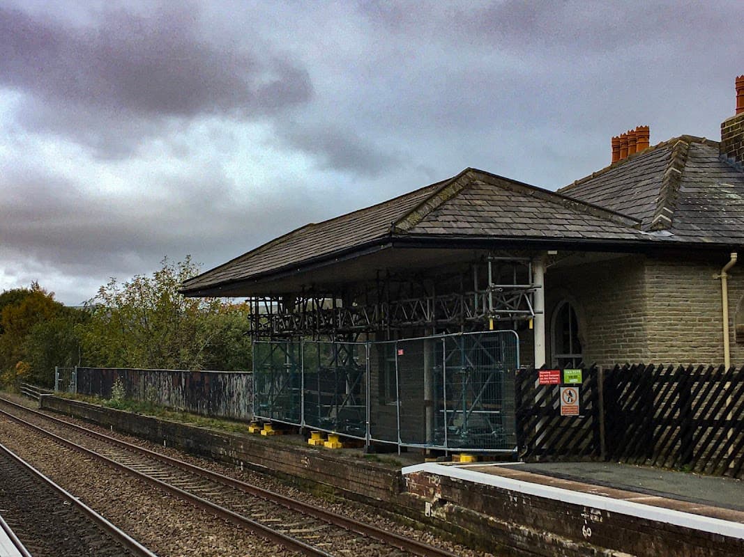 Mytholmroyd Station car park with scaffolding, railway tracks, and cloudy sky in Chiserley, Yorkshire.