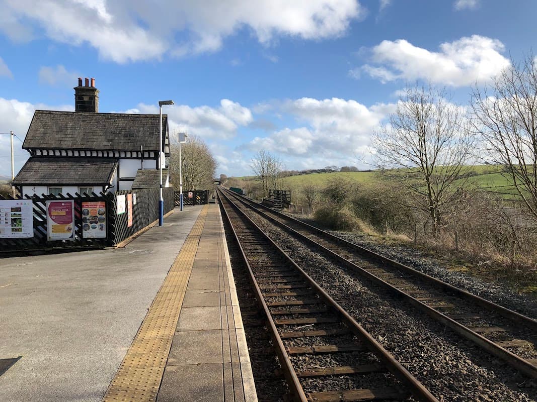 Railway tracks stretching into the distance beside a quaint station building under a blue sky with scattered clouds.