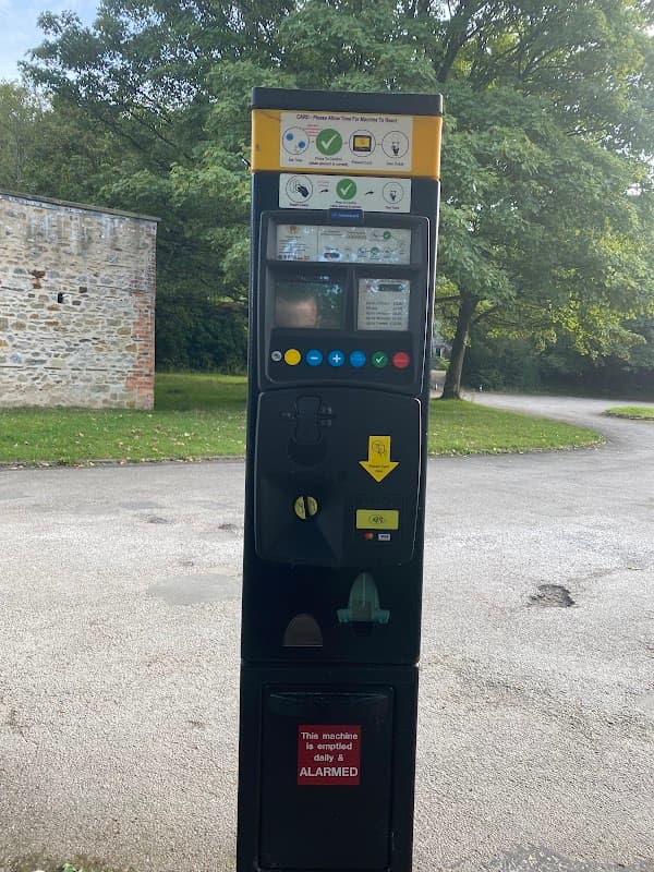 Parking machine with payment options, surrounded by greenery and a stone wall in Clapham, Yorkshire Dales National Park.
