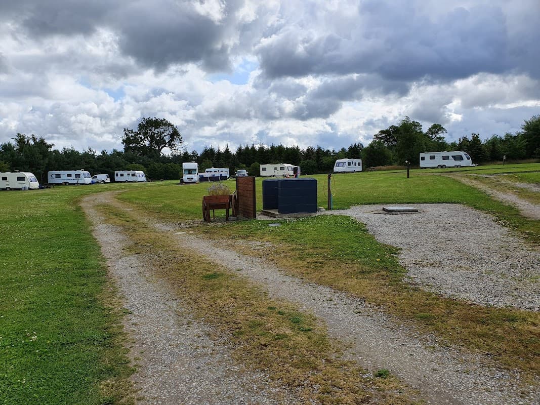 Caravan park with grassy areas, gravel paths, and several parked caravans under a cloudy sky.