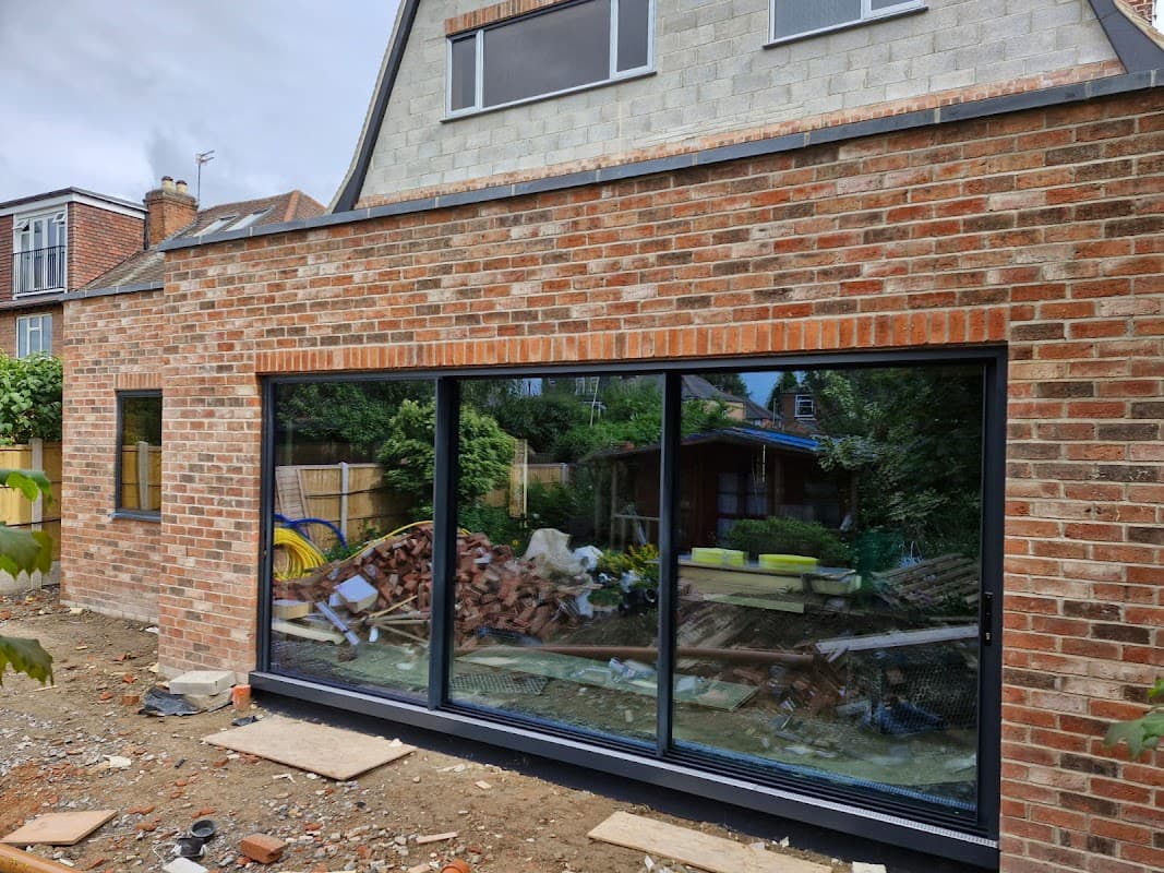 Large glass windows framed in black, set in a brick wall, overlooking a messy yard with construction materials.