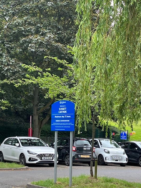 Free parking sign at Wakefield Road, Clayton West, with parked cars and trees in the background.