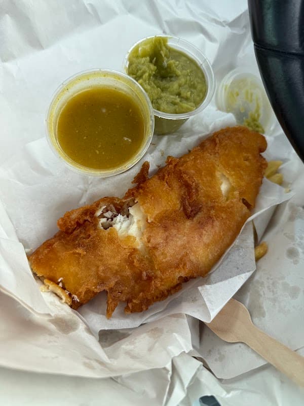 Crispy battered fish fillet with two sauces in cups, served on white paper.