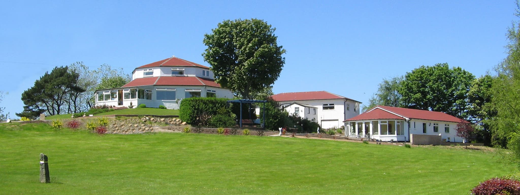 Harmony Country Lodge and Harmony Church set on a green hill, surrounded by trees and clear blue sky in Burniston, Yorkshire.