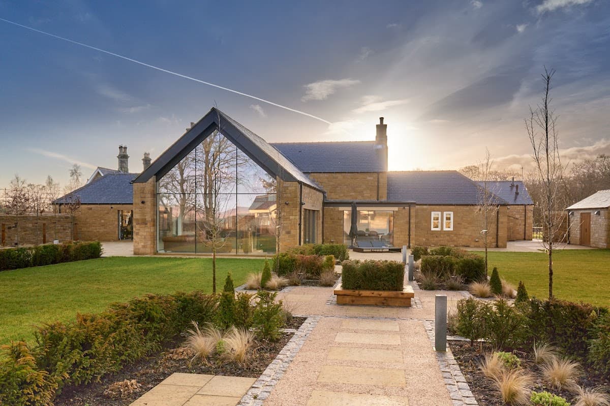Modern building with a sloped roof, large glass windows, surrounded by landscaped gardens and a stone pathway.