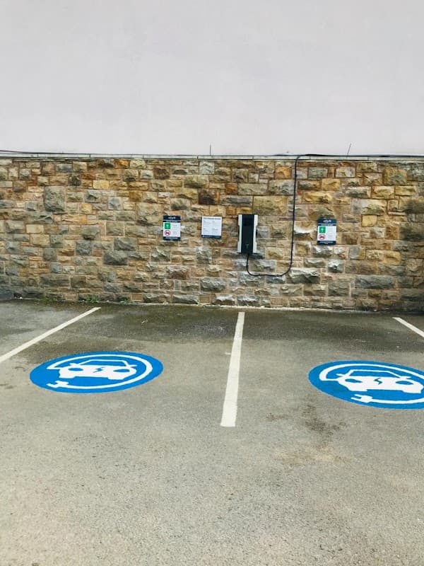 Alfa Power Charging Station with two charging points on a stone wall, marked parking spaces in blue with logos.