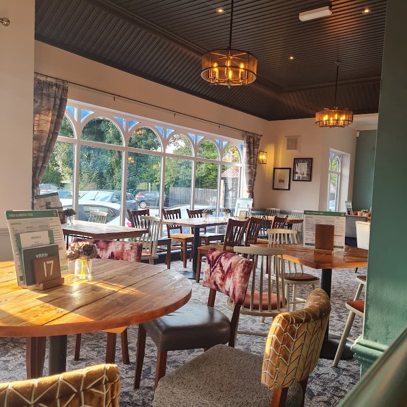 Cozy interior of Cromwell's Collingham with wooden tables, patterned chairs, and large windows letting in natural light.