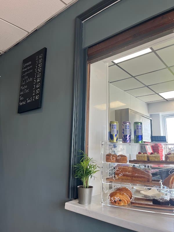 Menu board with coffee prices, a glass display case with pastries, and a small plant on a marble counter.