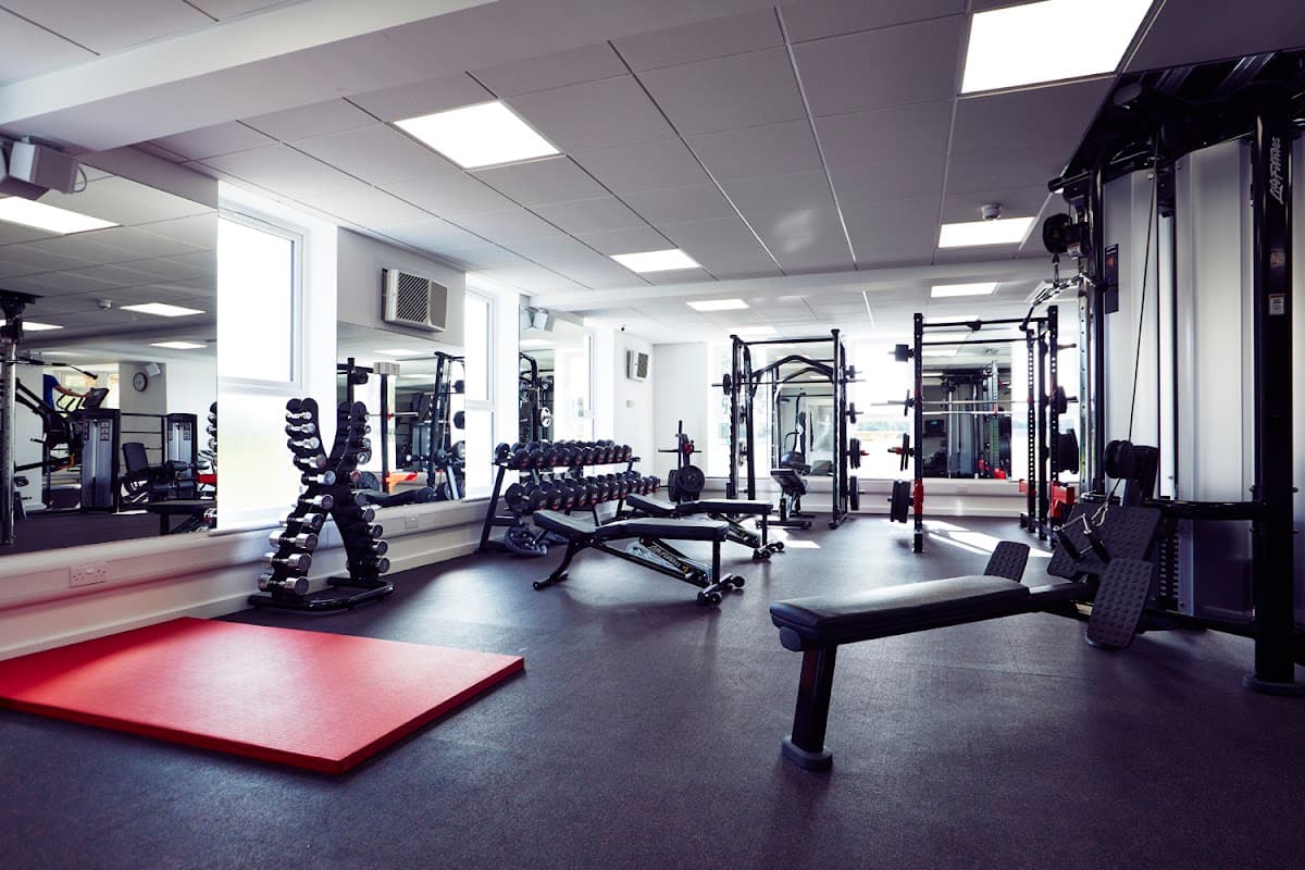 Modern gym interior featuring weightlifting equipment, benches, dumbbells, and a red exercise mat.