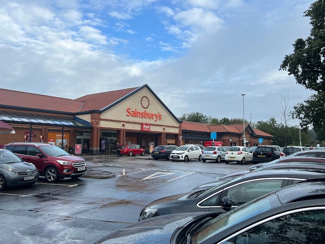 Sainsbury's storefront at Colton Retail Park, with parked cars and cloudy skies in the background.