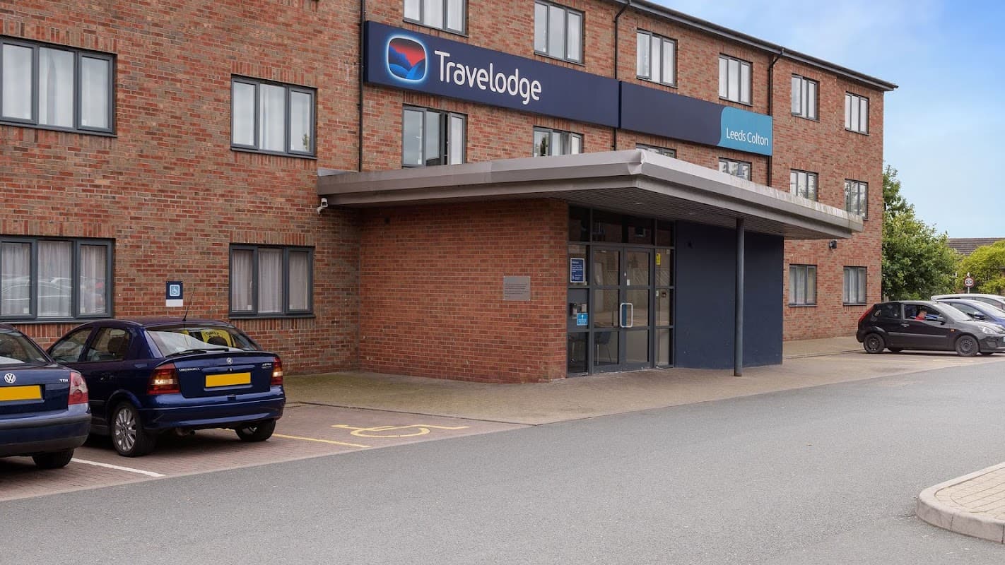 Travelodge Leeds Colton exterior with a brick facade, entrance, and parked cars in front.