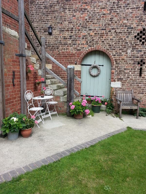 Charming outdoor seating area with white furniture, potted flowers, and a rustic door against a brick wall.