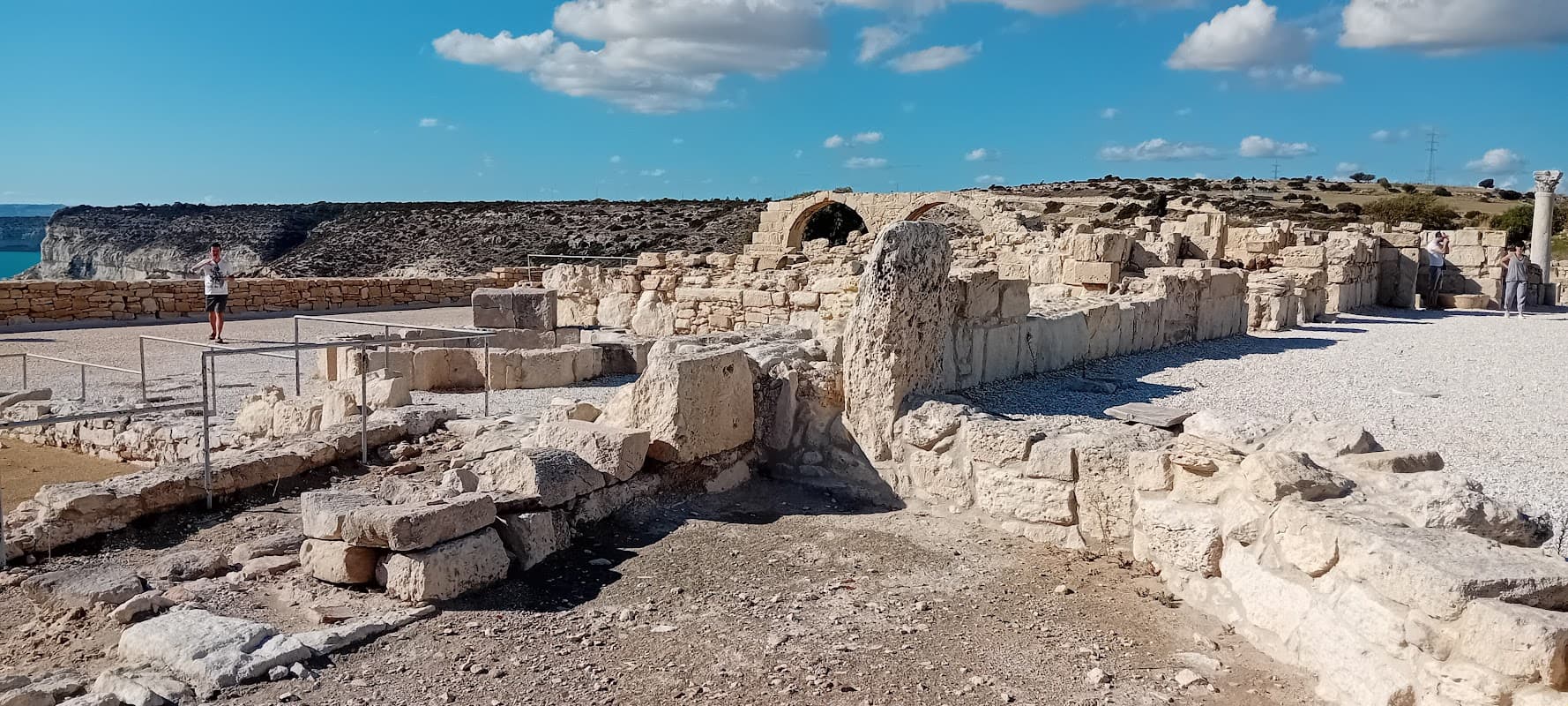 Ruins of stone structures with a clear blue sky and rocky landscape in the background.
