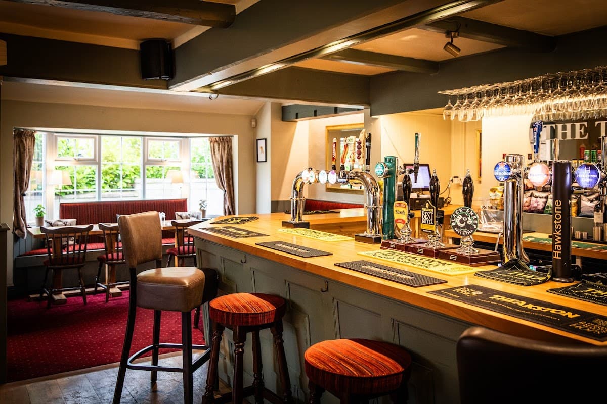 Warm interior of The Tiger Inn bar featuring wooden counter, stools, taps, and cozy seating area with natural light.