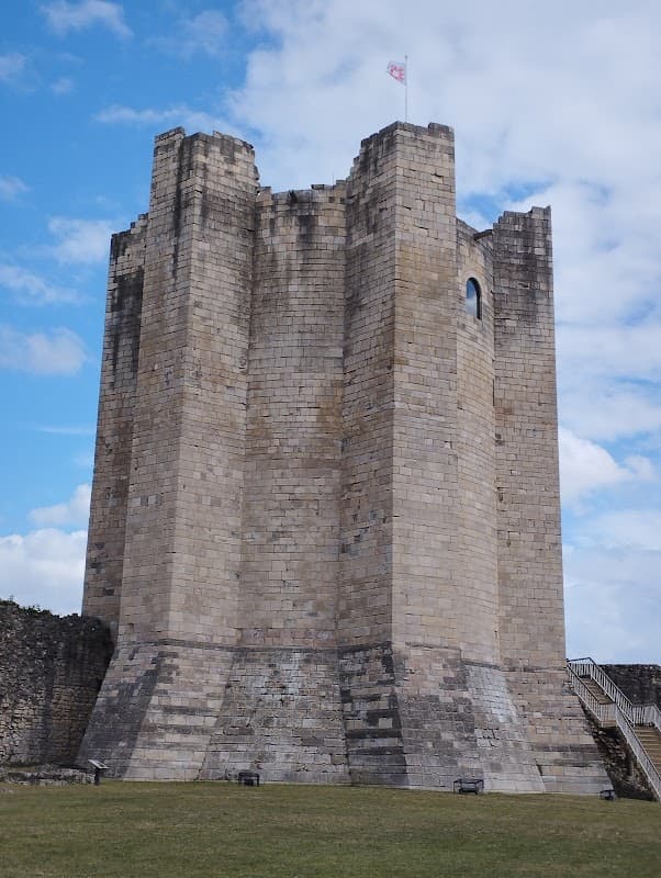 Conisbrough Castle's stone tower with a flag, set against a blue sky and grassy landscape.