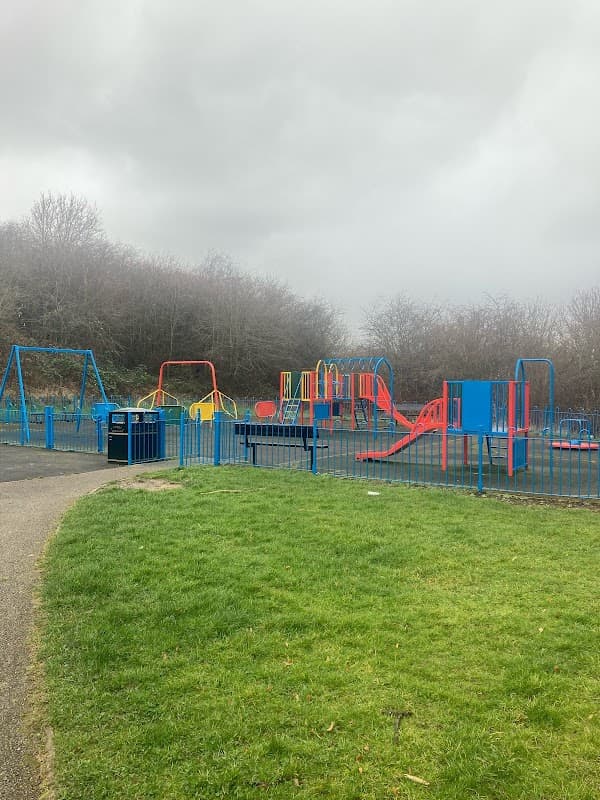Colorful playground equipment with swings, slides, and climbing structures, surrounded by green grass and trees.
