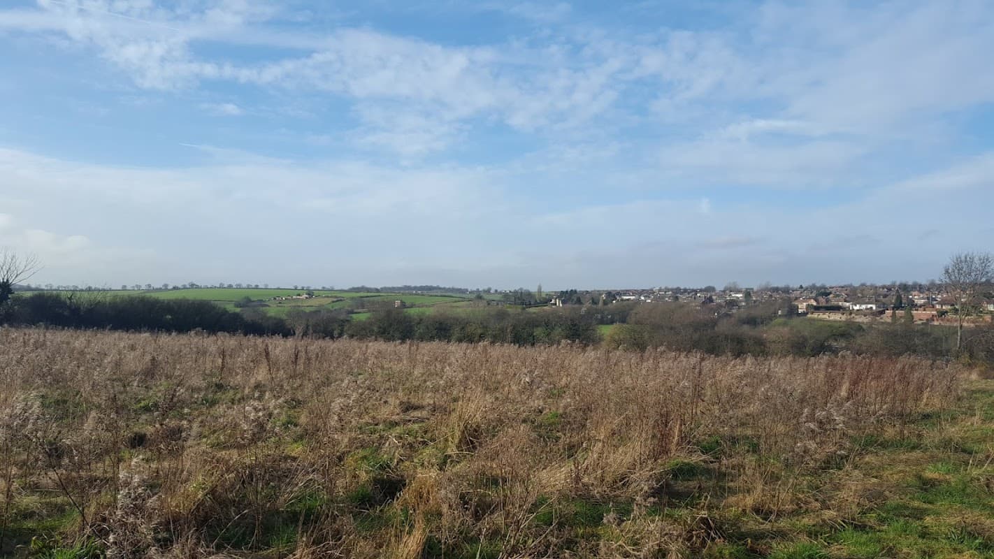 Expansive view of rolling hills and fields under a blue sky, with a distant village nestled among the greenery.