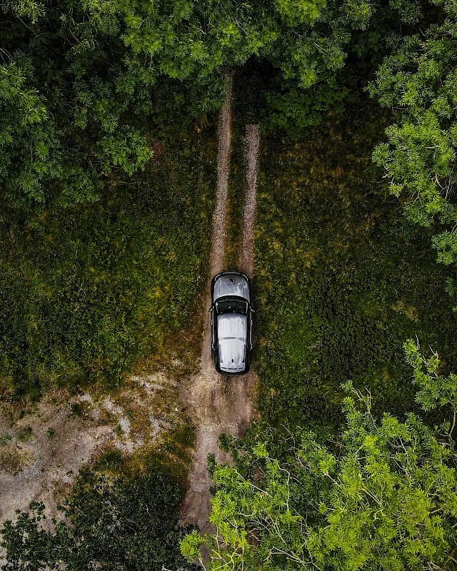 Aerial view of a black car parked on a dirt track surrounded by lush greenery in Coniston Off-Road Centre.
