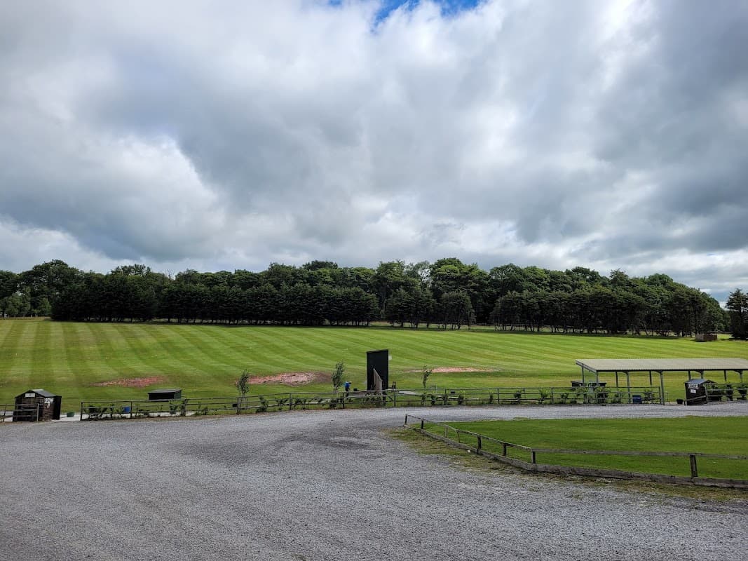 Green shooting grounds with neatly trimmed grass, trees in the background, and a cloudy sky overhead.