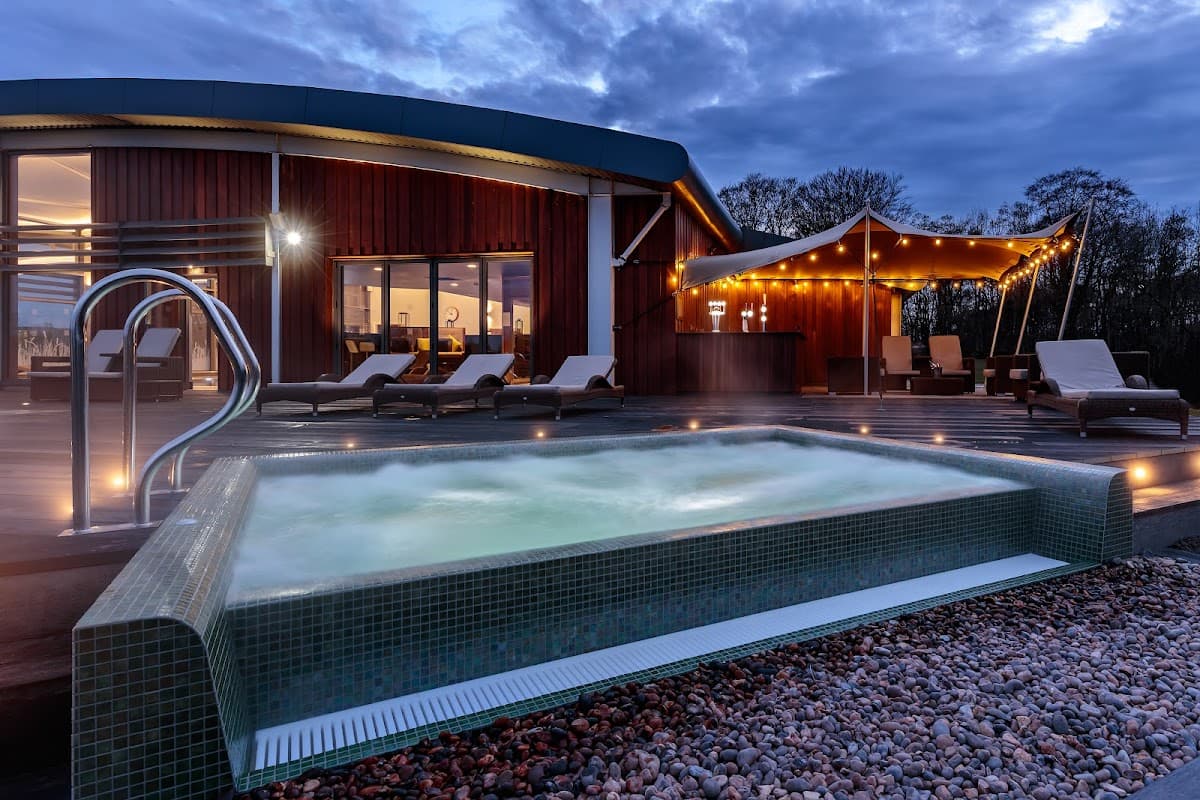 Outdoor spa with bubbling water, lounge chairs, and a modern building under a cloudy sky at The Coniston Hotel.