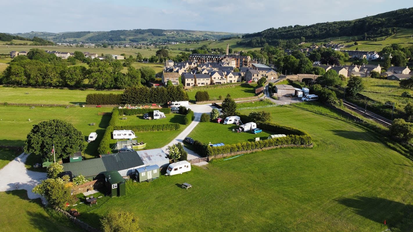 Aerial view of Riverside Hotel in Cononley, surrounded by greenery, with caravans and hills in the background.