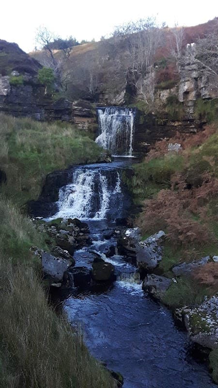Waterfall cascading down rocky terrain, surrounded by lush greenery and autumn foliage in Cotterdale, Yorkshire.
