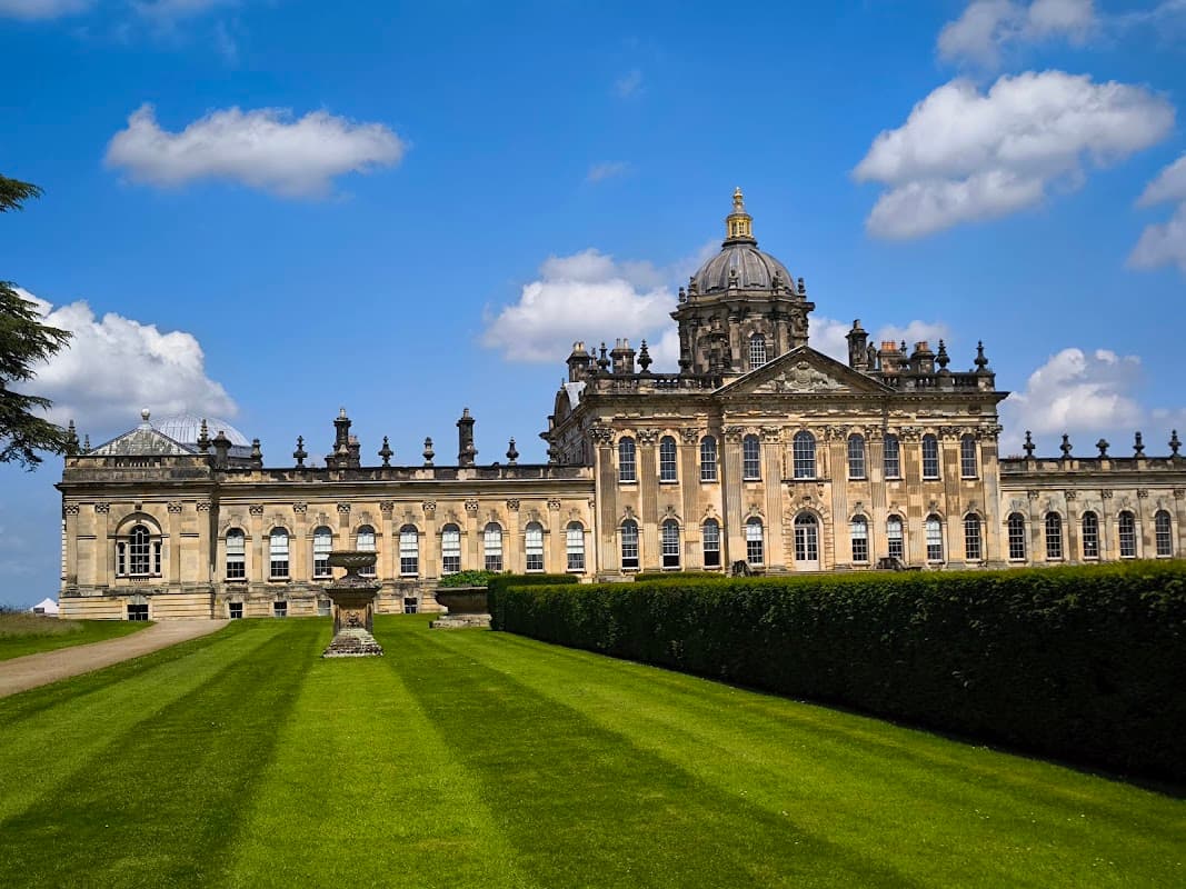 Historic grand building with ornate architecture, surrounded by lush green lawns and a clear blue sky.