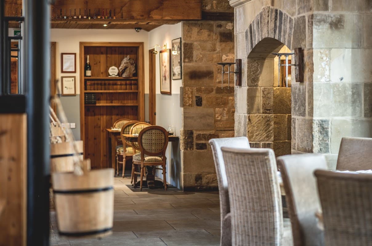 Cozy dining area with stone walls, wooden beams, and rustic furniture at The Saddle Room Restaurant in Coverham.