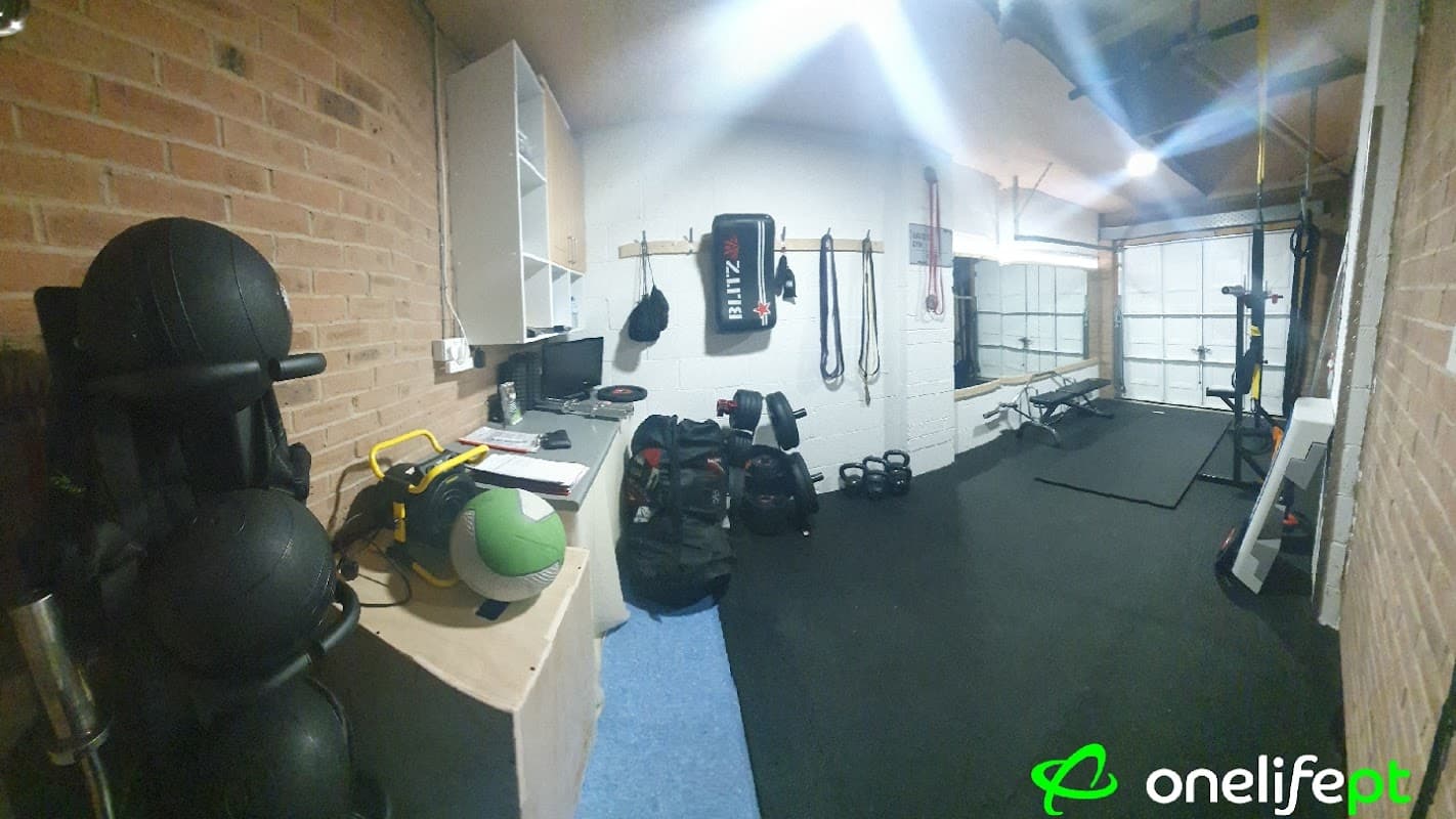 Personal training space with weights, exercise equipment, and a boxing bag in a well-lit, brick-walled environment.