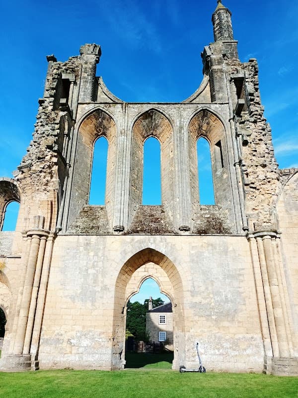 Ruins of a historic stone building with large arched windows under a bright blue sky, surrounded by green grass.