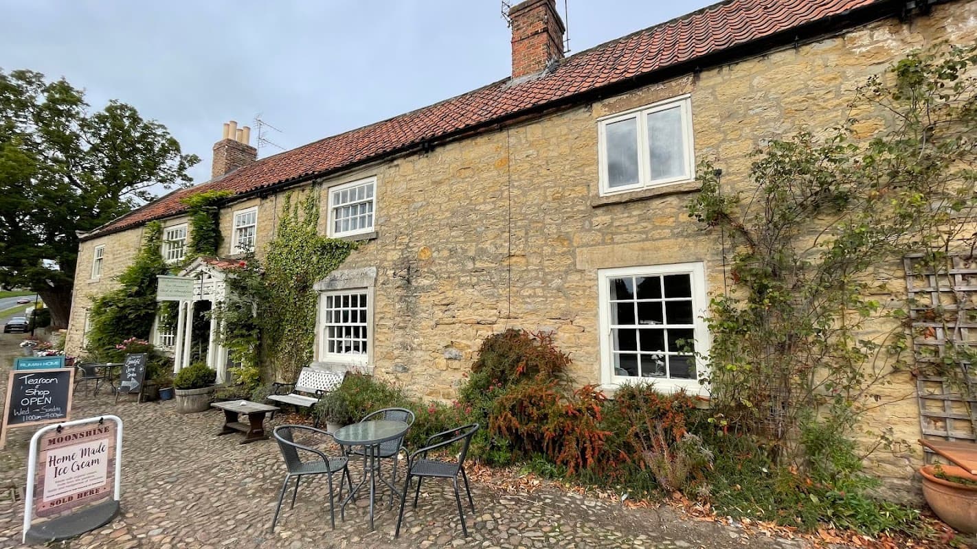 Charming stone building with a red-tiled roof, outdoor seating, and lush greenery in Coxwold, Yorkshire.