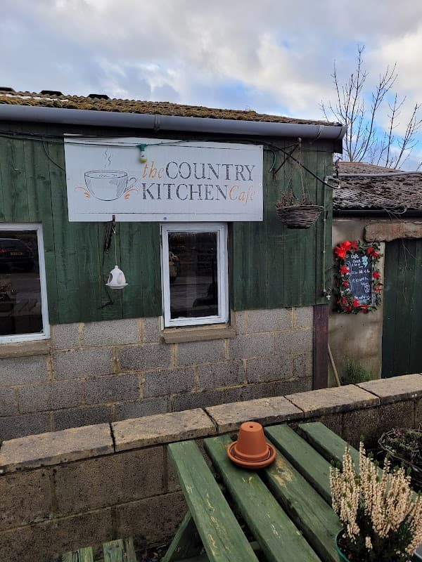 The Country Kitchen Café sign on a green wooden building with a flower pot and seasonal decorations nearby.