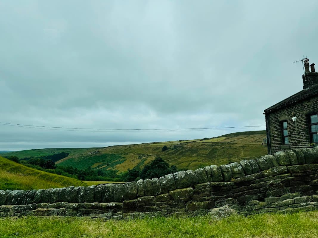 Stone wall in foreground with a view of rolling green hills and a cloudy sky in Cragg Vale, Yorkshire.