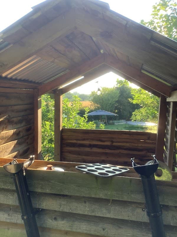 Wooden structure with a sloped roof, featuring open windows and a view of greenery in the background.