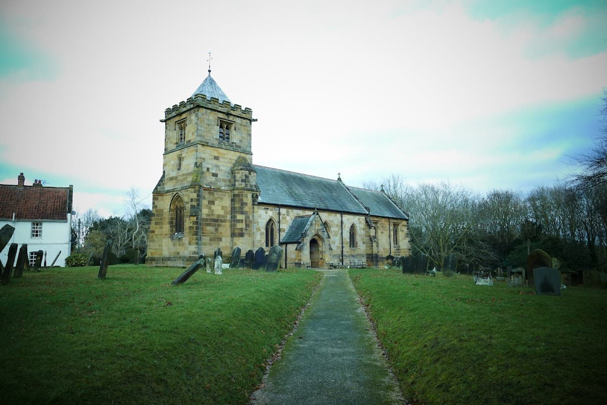 Historic stone church with a tall tower, surrounded by gravestones and trees in a rural setting.