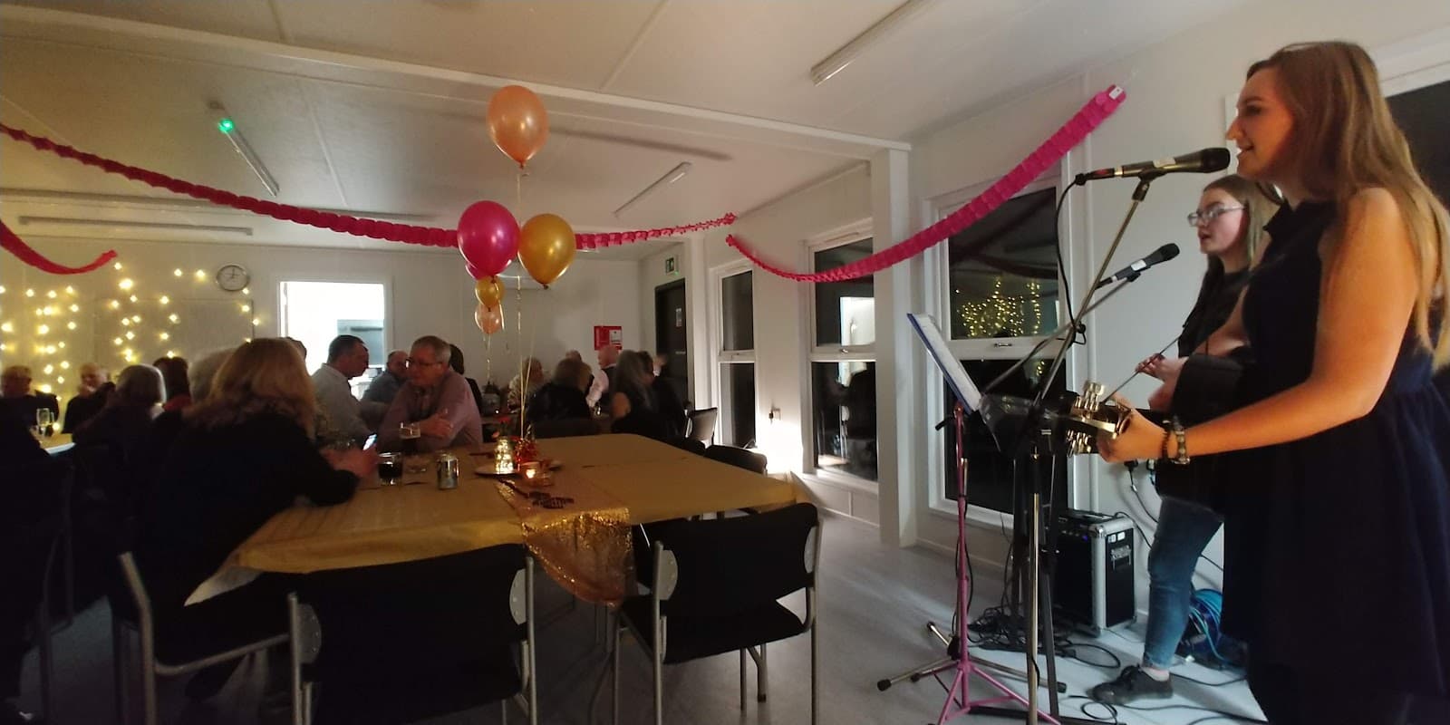 A lively event in Croft Village Hall with musicians, balloons, and guests enjoying a festive atmosphere.