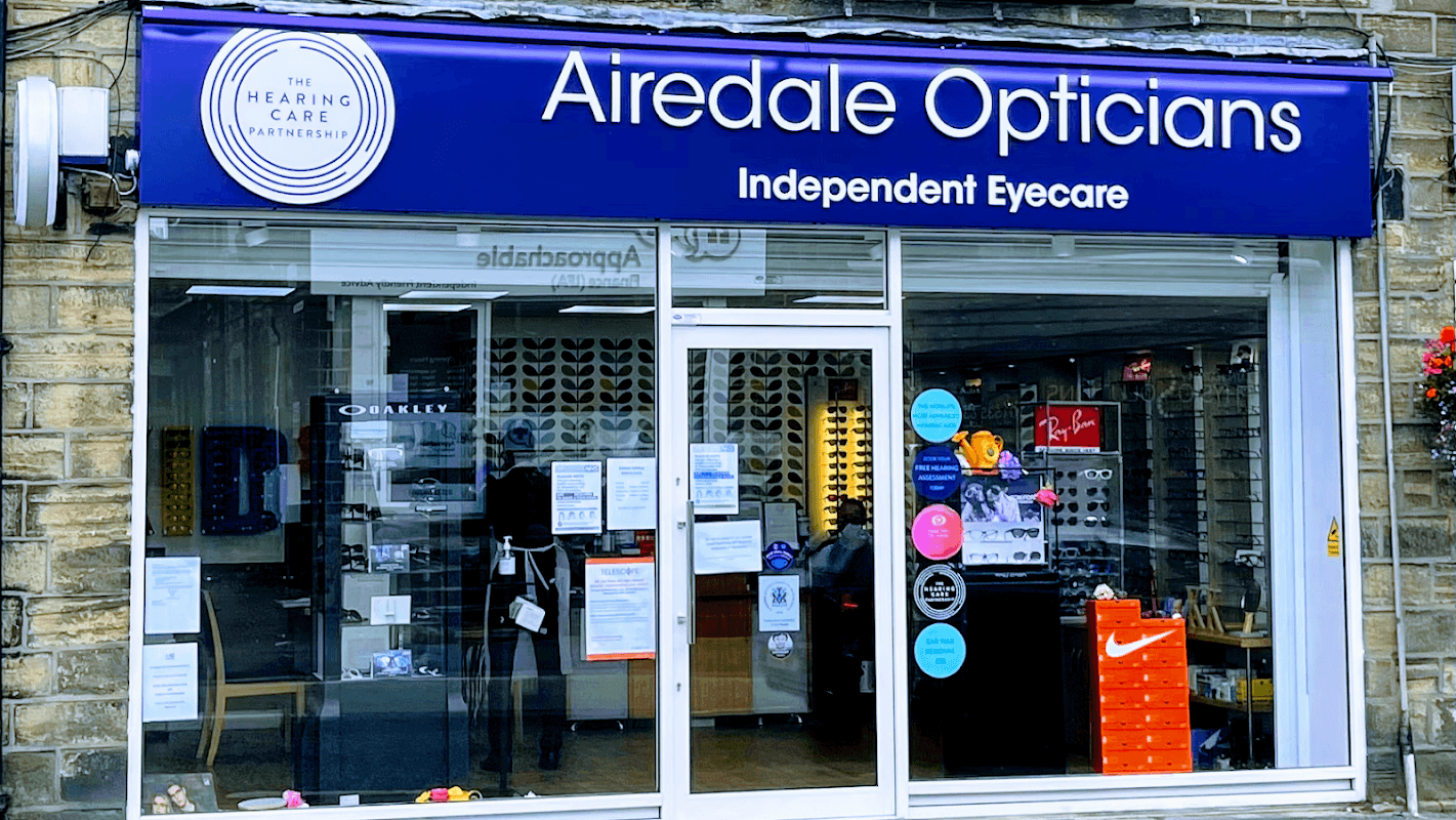 Airedale Opticians storefront featuring blue signage, eyeglasses displays, and colorful promotional signs.