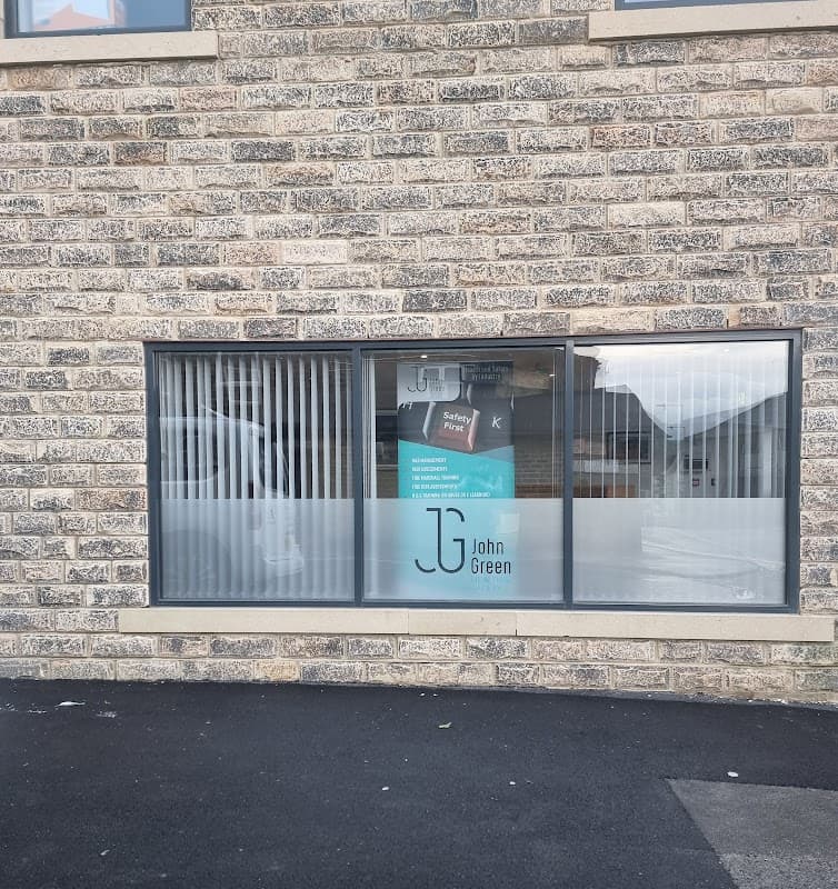 Window display featuring "John Green Health And Safety" signage on a stone building in Cross Hills, Yorkshire.