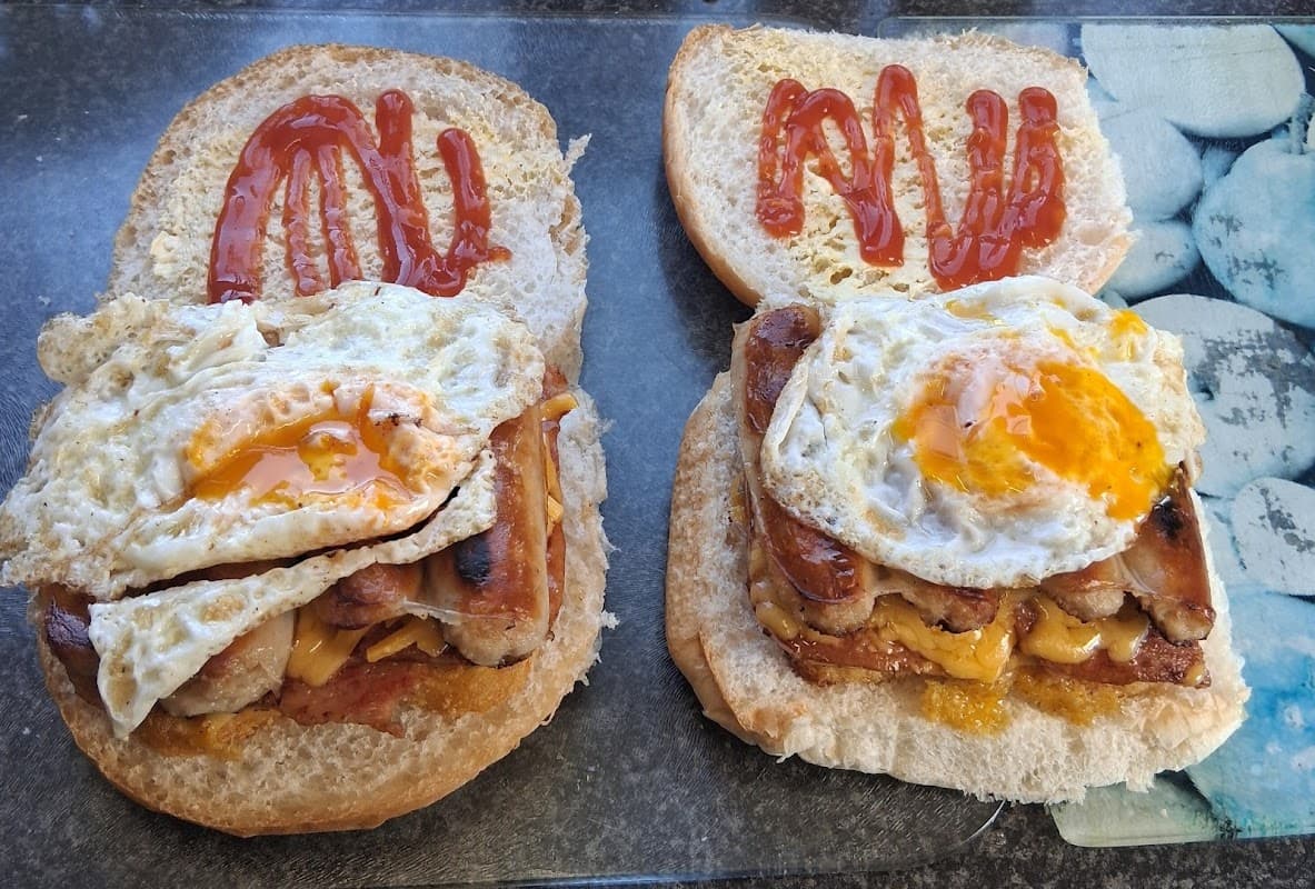 Two sandwiches with fried eggs, melted cheese, and sausage, topped with ketchup on a gray countertop.