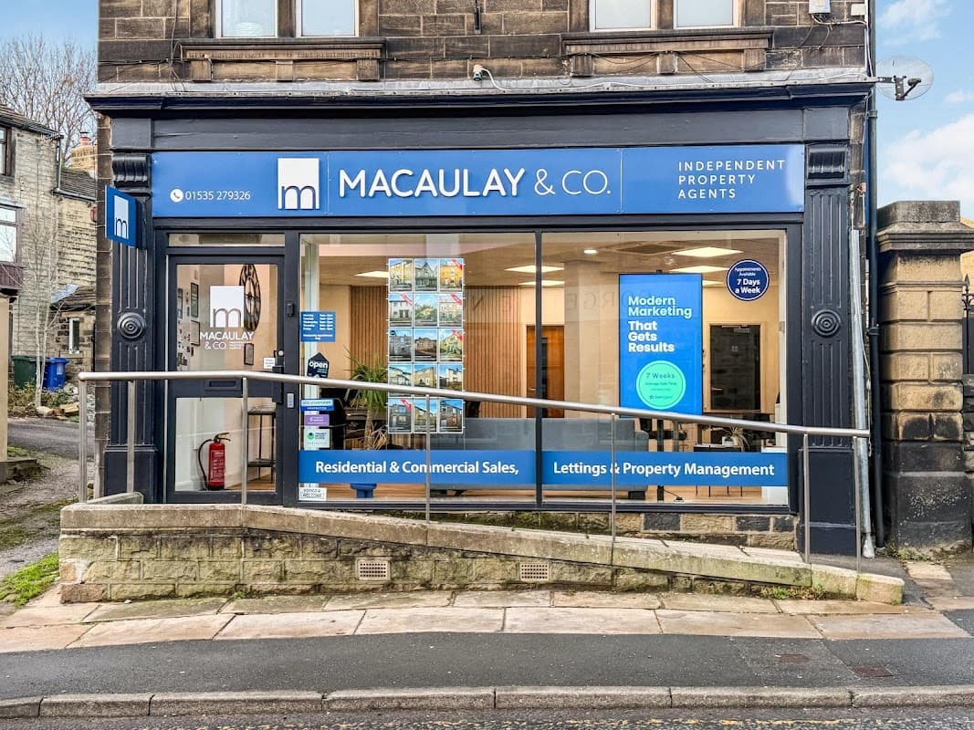 Macaulay & Co. storefront in Cross Hills, featuring a blue sign, large windows, and promotional posters inside.