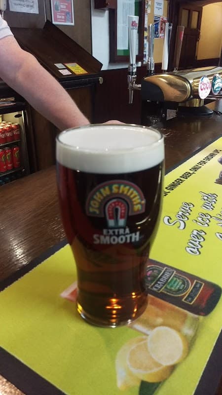 Pint of John Smith's Extra Smooth on a bar counter with drinks and promotional signage in the background.