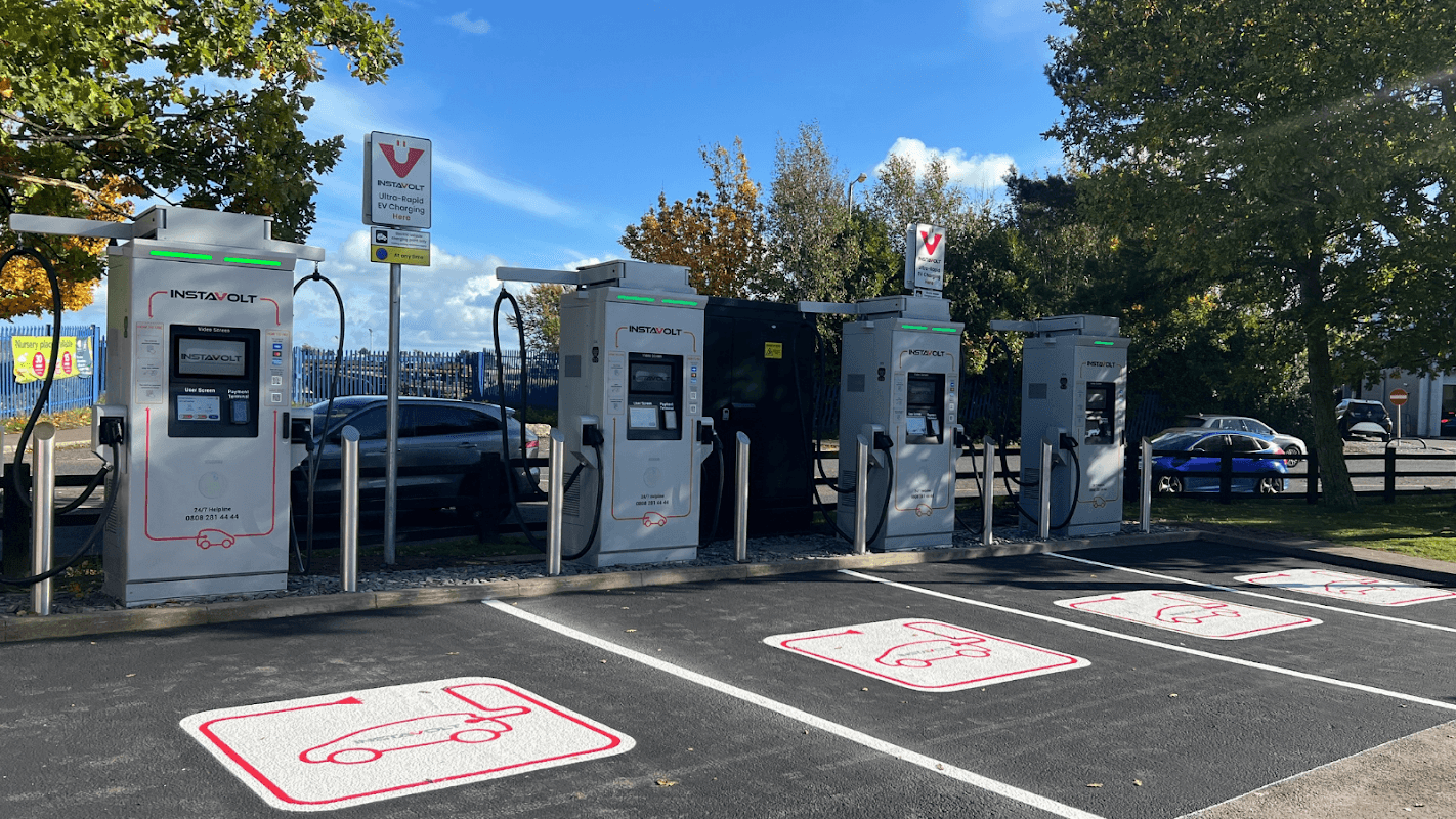 InstaVolt charging station with multiple chargers, parking spaces marked for electric vehicles, and trees in the background.