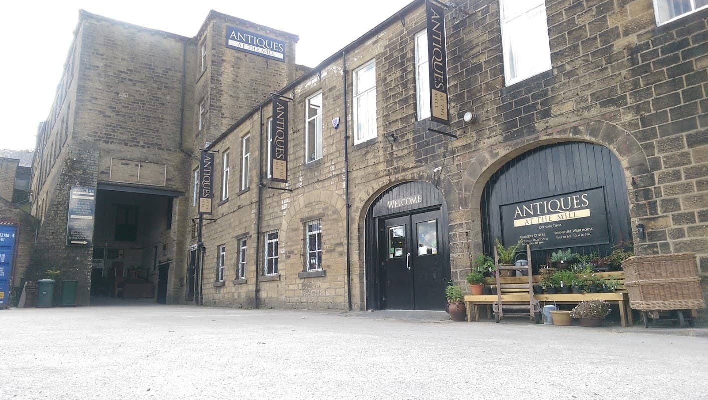 Historic stone building with signage for "Antiques at the Mill" and potted plants near the entrance.