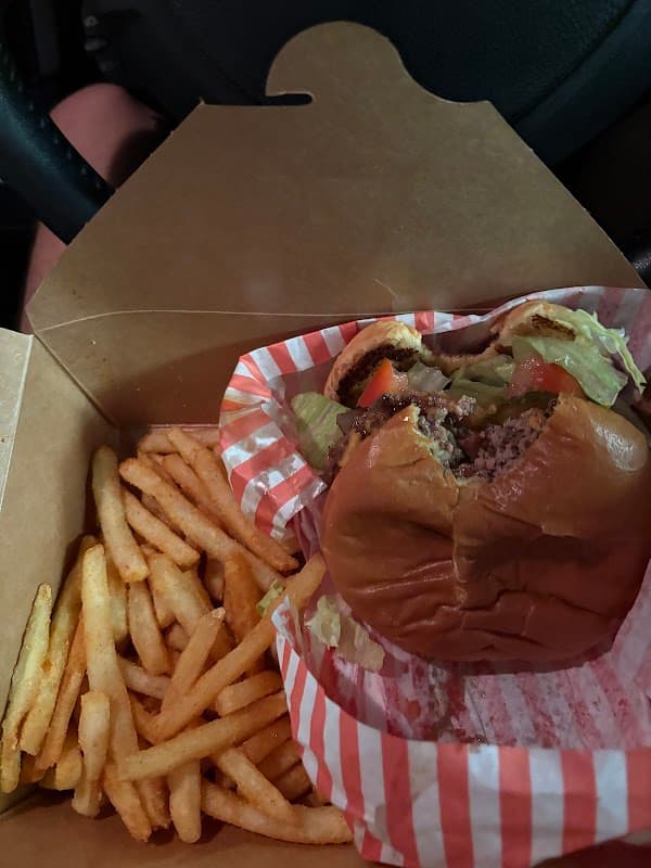 A takeout box containing a half-eaten burger with lettuce and tomato, alongside a serving of fries.