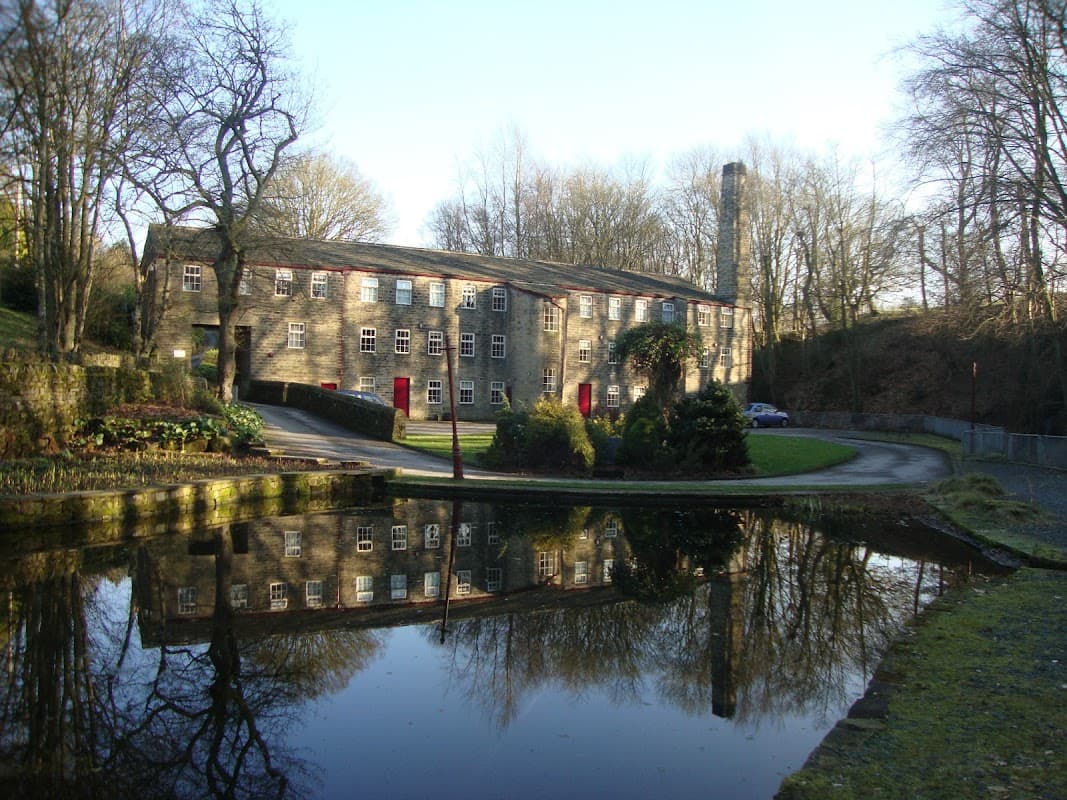 Historic stone cottages and apartments beside a tranquil pond, surrounded by trees in Cullingworth, Yorkshire.