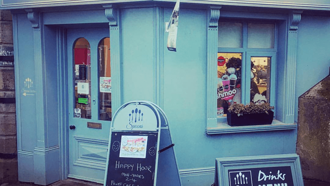 Blue restaurant exterior with a sign for "Happy Hour" and a window displaying food items.
